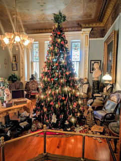 Decorated Christmas tree in a Victorian-era parlor with ornate ceiling and antique furnishings