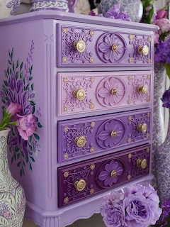 Ornate purple chest of drawers with carved floral designs, gold knobs, and painted flowers