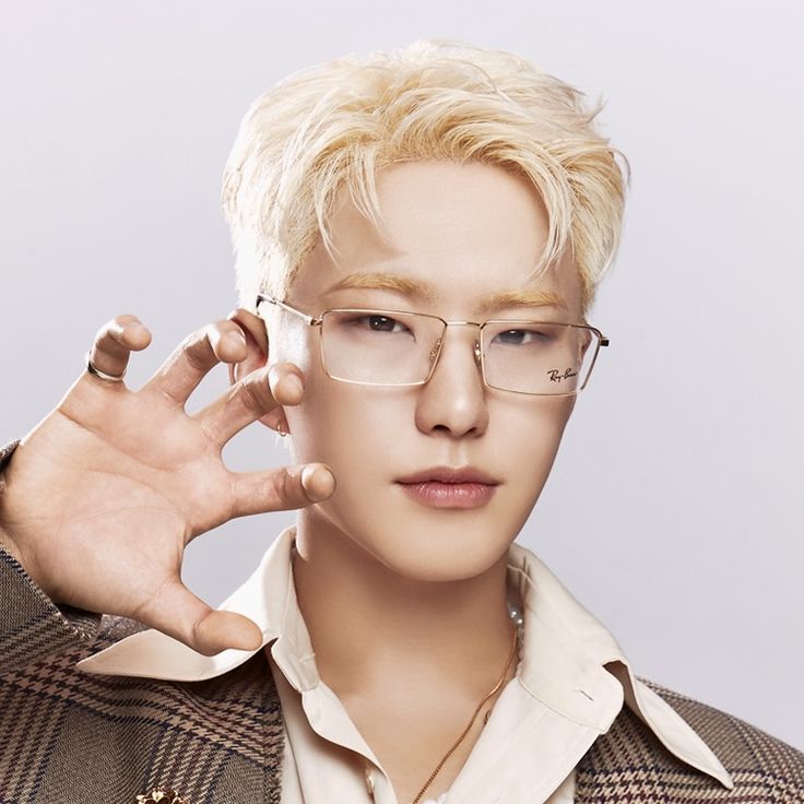 Studio portrait of a blond young man in glasses and a checkered jacket with his hand raised