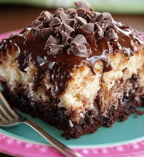 Close-up of a chocolate cake square with glossy frosting and chocolate curls on a turquoise plate.