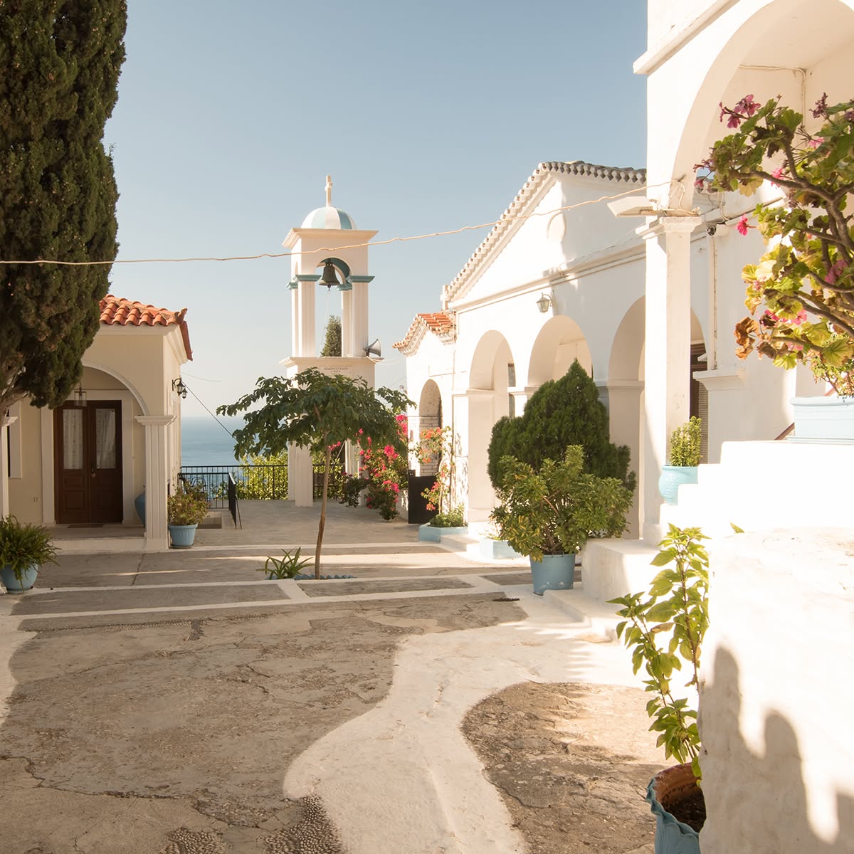 White church buildings and a bell tower in a sunny Greek village courtyard