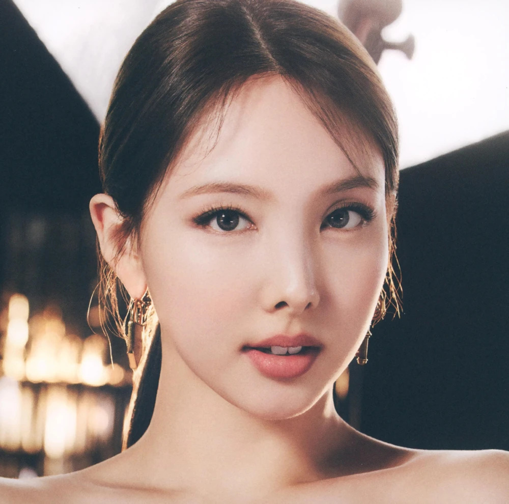 Close-up portrait of Nayeon with earrings and a warm blurred background