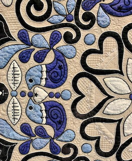 Close-up of a blue, white, and black quilt with heart and paisley patchwork patterns