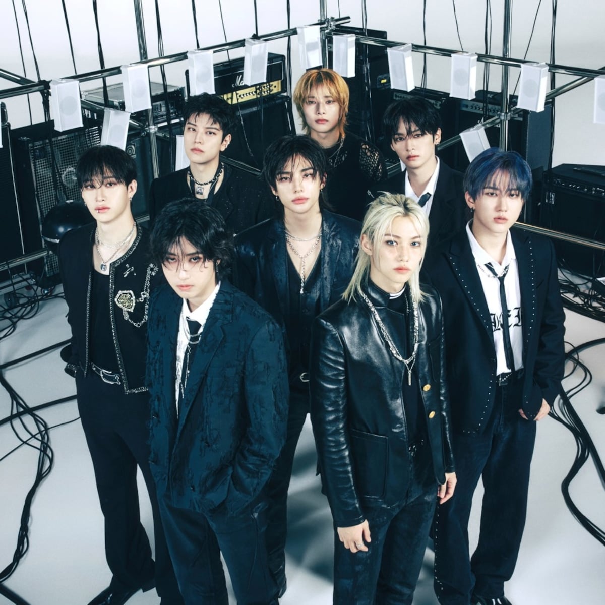 Seven young men in black outfits posing in a studio with cables and equipment