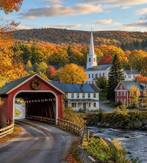 Red covered bridge and white church steeple in a Vermont village with autumn trees by a river