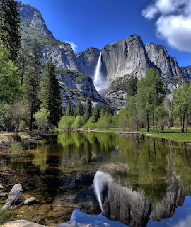 Yosemite Falls and granite cliffs reflected in a calm river with pine trees and blue sky