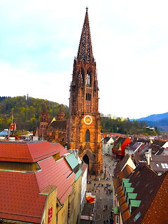 Freiburg Minster gothic cathedral spire towering over old town roftops with green hills behind