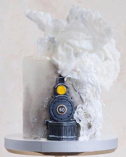 Steam train themed cake with white frosting smoke on a white cake stand