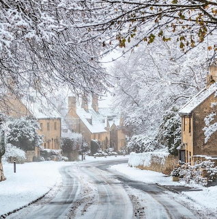 Snowy village street with stone cottages and frosted tree branches in winter Cotswolds