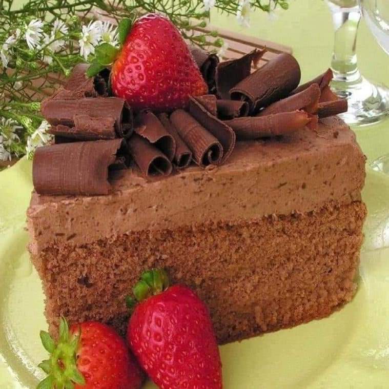 Chocolate cake slice with chocolate curls and strawberries on yellow plate