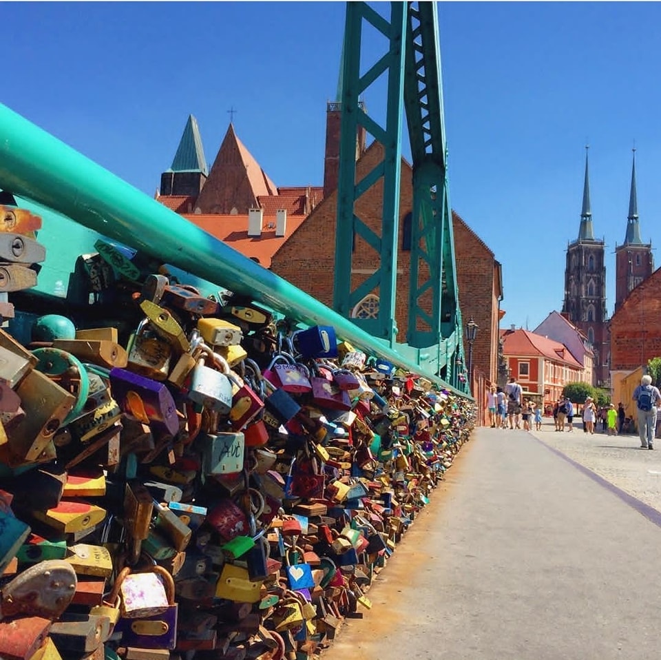 Colorful love locks on a bridge railing in Wrocław with church towers in the background