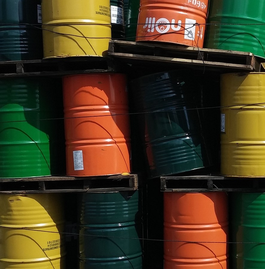 Stacks of colorful steel drums on pallets, including green, yellow, orange, and dark blue barrels