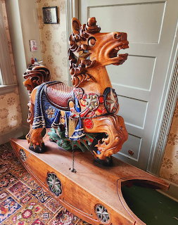 Ornate wooden carousel horse with painted saddle on antique cabinet