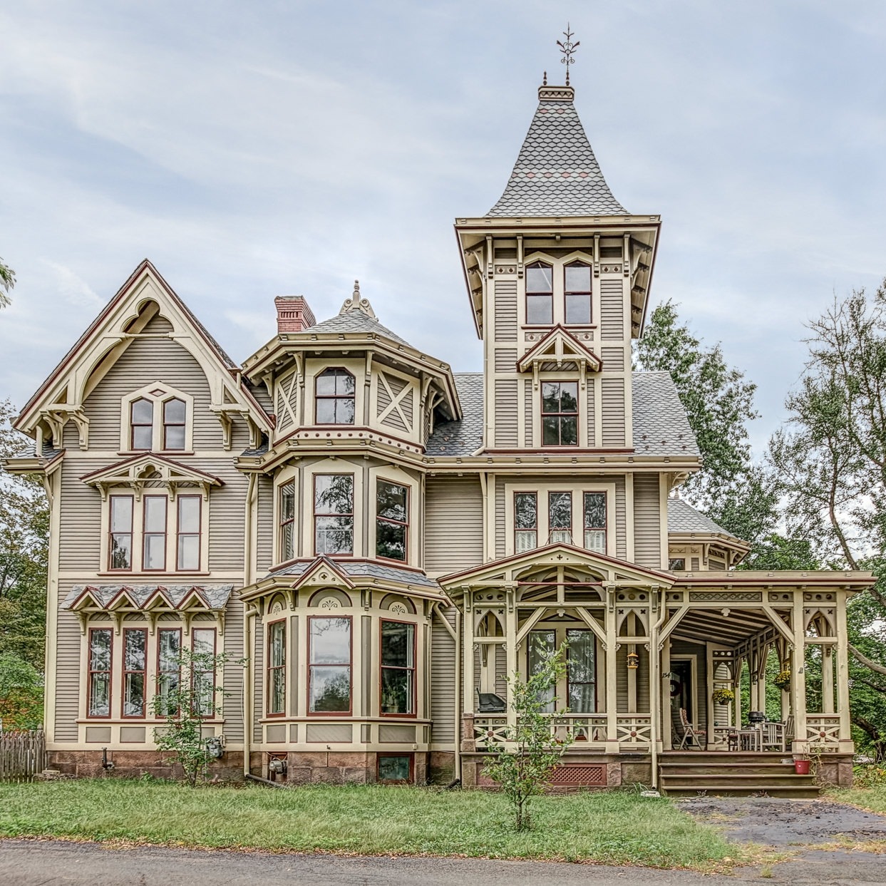 Ornate Victorian Gothic mansion with tall tower and wraparound porch on overcast day