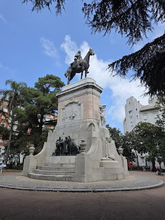 Bronze equestrian statue monument in sunny urban plaza surrounded by trees