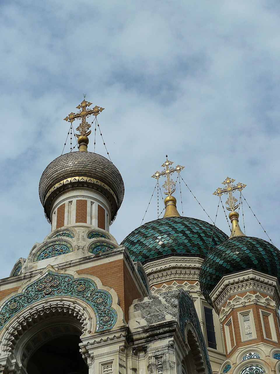 Golden and green onion domes of a Russian Orthodox church with ornate crosses under a cloudy sky