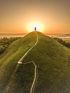 Stone tower on grassy hilltop with winding paths at sunset