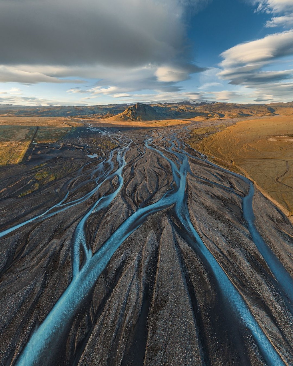 Aerial view of bright blue braided rivers cutting through dark volcanic landscape in Iceland