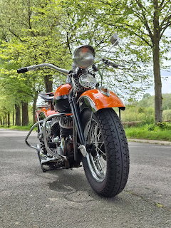 Orange and black 1943 Harley-Davidson WLC military motorcycle on a paved road with green trees in background