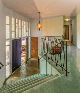 Green carpeted staircase with ornate iron railing in a home interior with French doors and pendant light