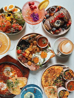 Overhead flat lay of various breakfast dishes including pancakes, fruit bowls, eggs, and coffee on white background