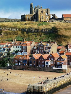 Seaside village houses below old abbey ruins on a grassy hill above a sandy beach