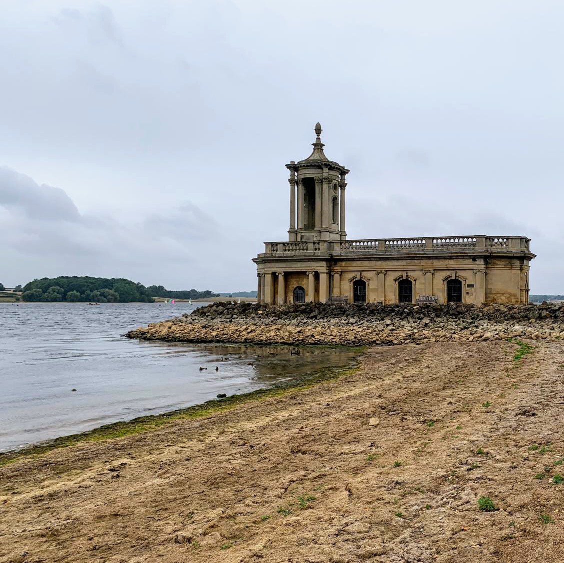 Stone church building on a narrow peninsula extending into a large lake on an overcast day