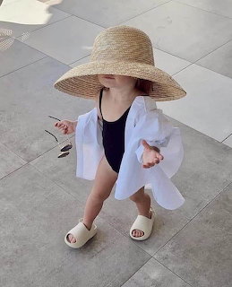 Young girl in straw hat and white shirt standing on pavement, viewed from above