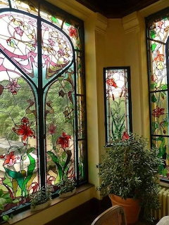 Art Nouveau stained glass windows with colorful floral designs and potted plants in yellow interior corner