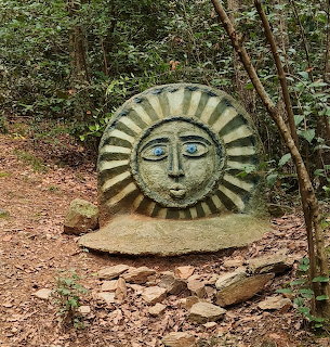 Stone sun face sculpture beside a rocky forest path in the woods