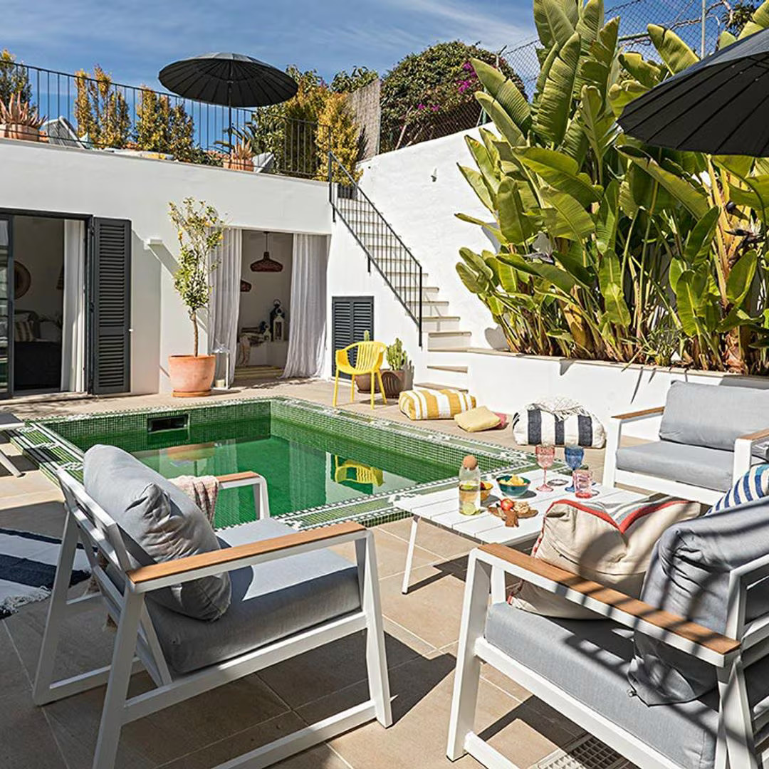 Modern white terrace with small turquoise pool, lounge chairs, tropical plants, and exterior staircase