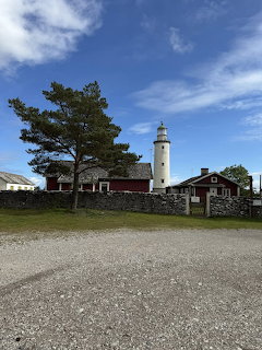 White lighthouse with red cottages and stone walls under a blue sky with scattered clouds