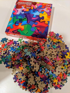 Colorful jigsaw puzzle box with rainbow pieces and scattered assembled puzzle pieces on white surface