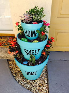 Three stacked turquoise pots reading Home Sweet Home with succulents and flowers on a porch