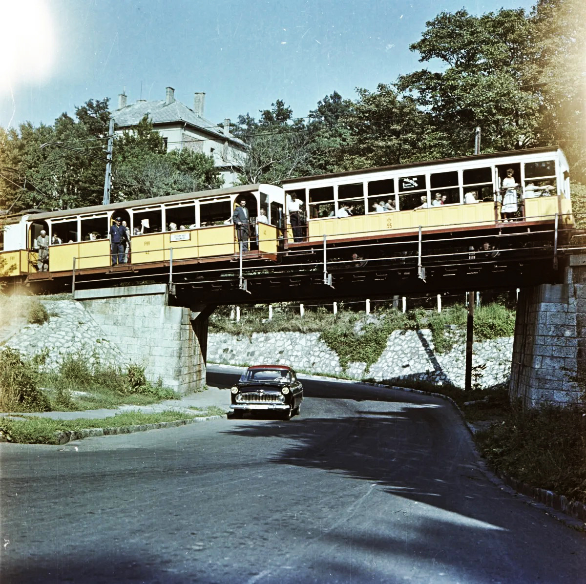 Yellow tram crossing bridge over road with vintage car in Budapest, 1960s photograph