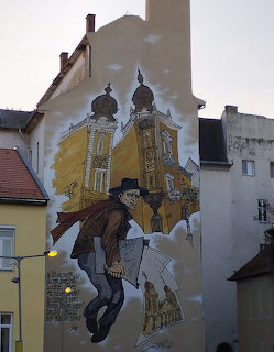 Street art mural on building wall showing a man in hat and coat with golden church domes in Debrecen, Hungary