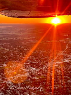 Aerial view from airplane window showing bright sunset over city with dramatic orange sky and sun rays
