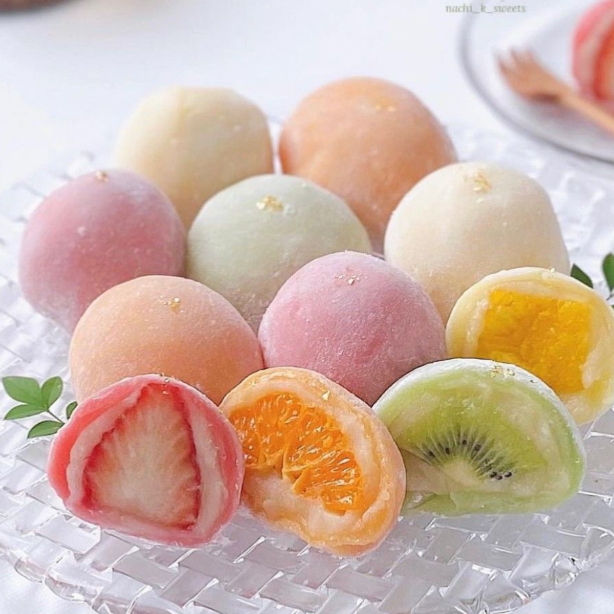 Assorted pastel mochi on a glass plate, with cut pieces showing fruit fillings like strawberry, orange, kiwi, and mango