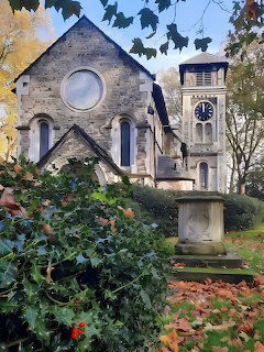 Stone church with round window and clock tower surrounded by green ivy and autumn trees