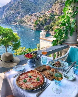 Pizza and drinks on a terrace table overlooking a colorful Italian coastal town and turquoise sea