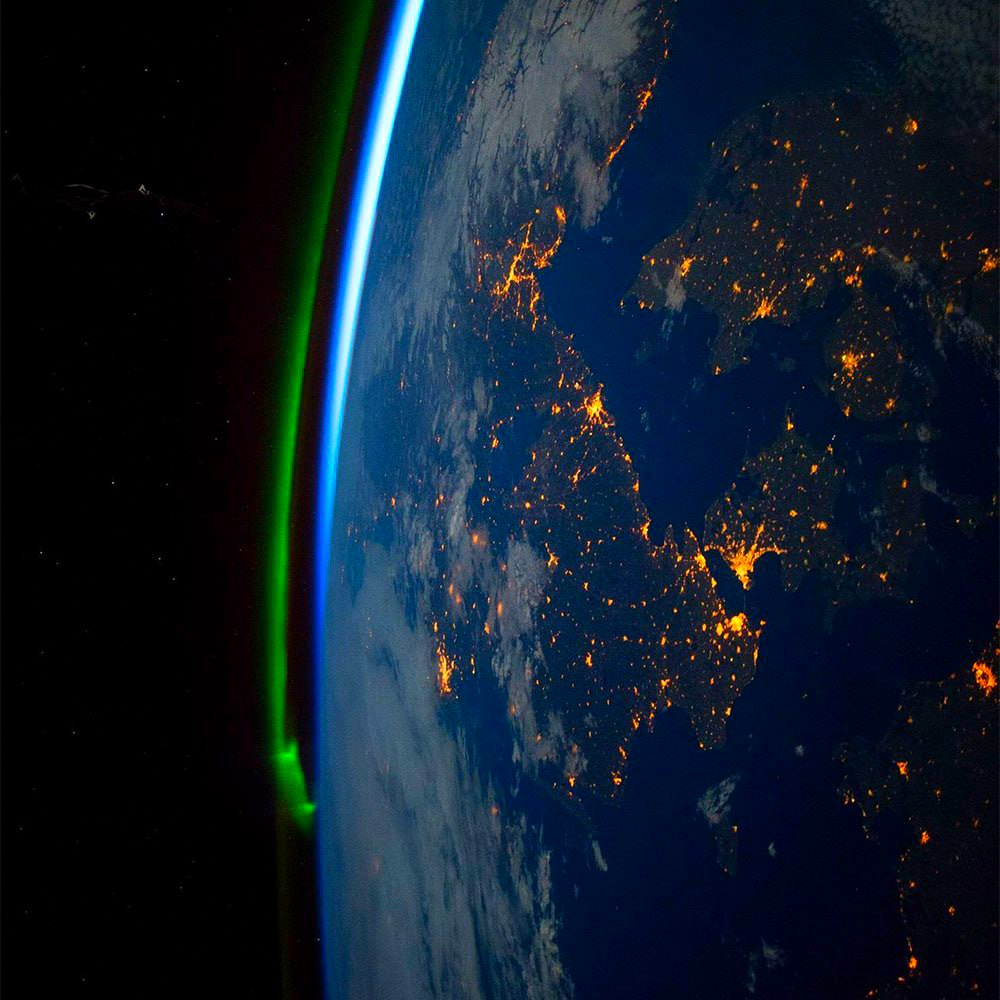 Earth from space showing illuminated cities at night with glowing atmosphere and stars in black sky