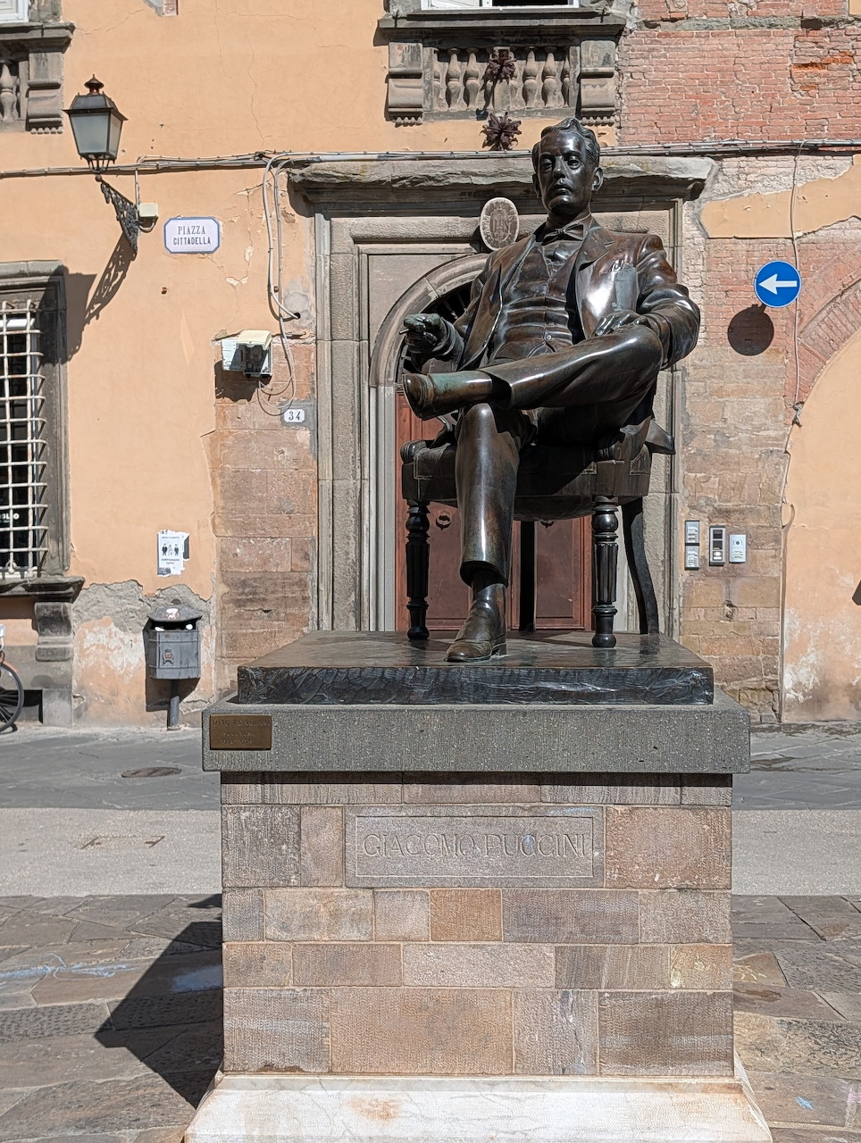 Bronze statue of seated Giacomo Puccini on stone pedestal in Italian plaza