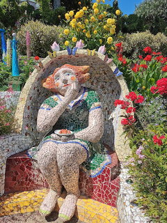 Seated mosaic girl sculpture in a flower-filled garden