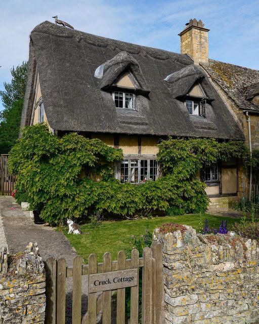 Thatched stone cottage with ivy, dormer windows, and a small garden behind a gate