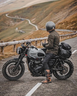 Motorcyclist on Triumph motorcycle parked at mountain overlook with winding road through hills