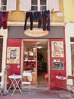 Red-fronted chocolate shop in Marseille with bistro table and laundry hanging from windows above