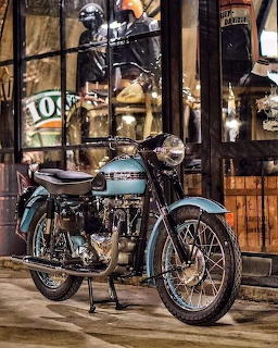 Vintage Triumph motorcycle with chrome engine parked outside an old-fashioned shop at night