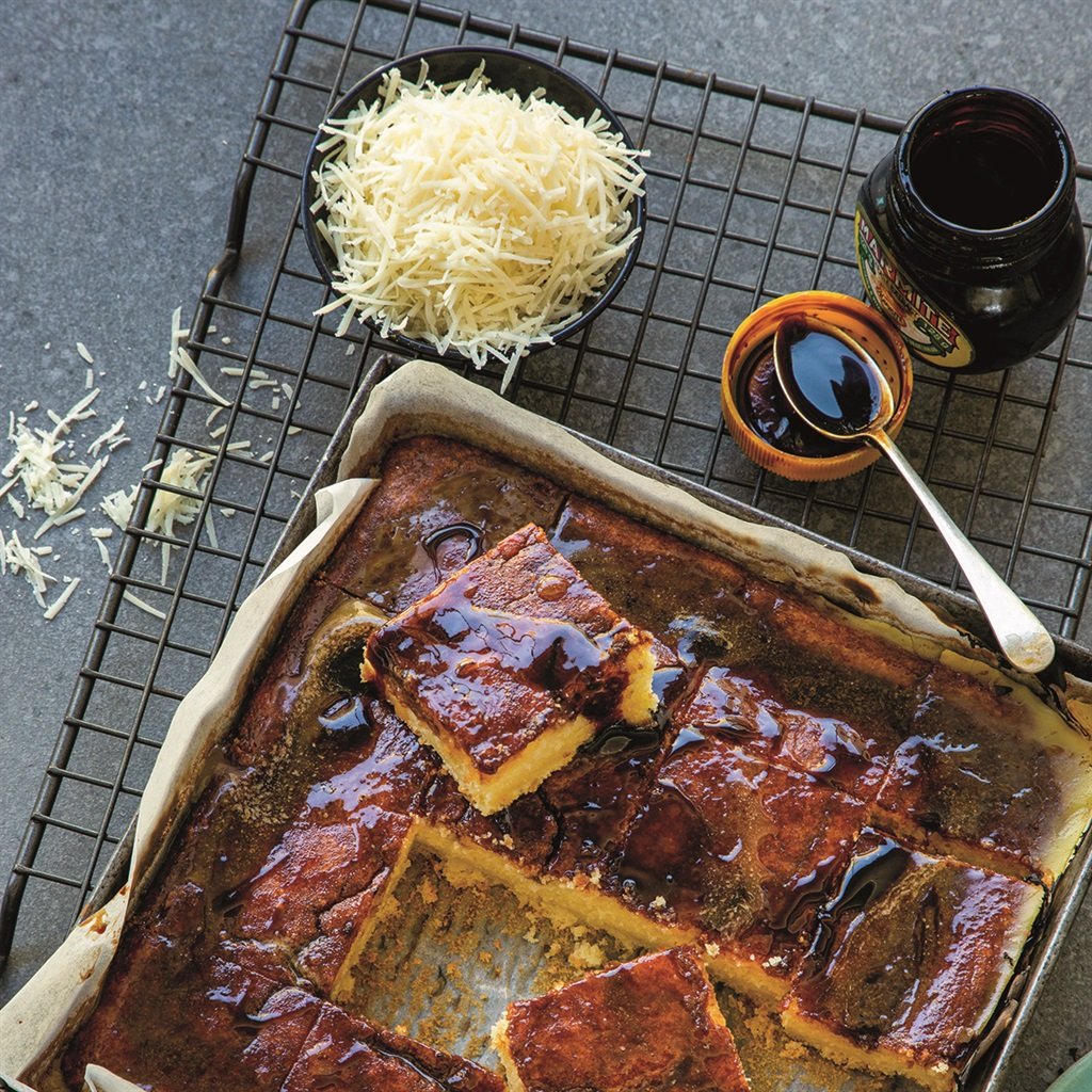 Overhead view of marmite tray bake squares with grated cheese and an open jar beside the pan