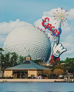 Epcot's Spaceship Earth geodesic dome with Mickey Mouse wand and Epcot sign at entrance plaza by lake