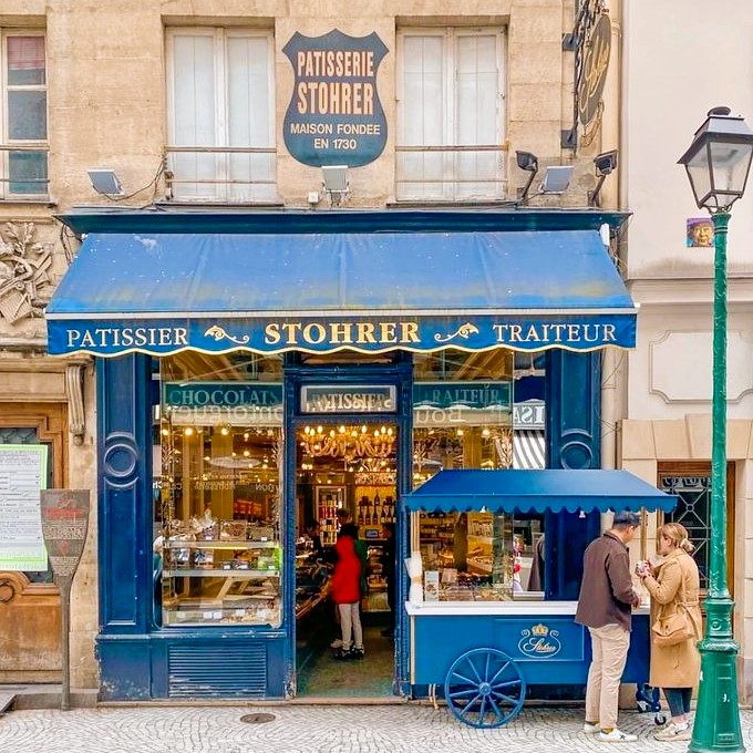 Blue Parisian patisserie shop front with ornate gold lettering, display windows, and vintage cart